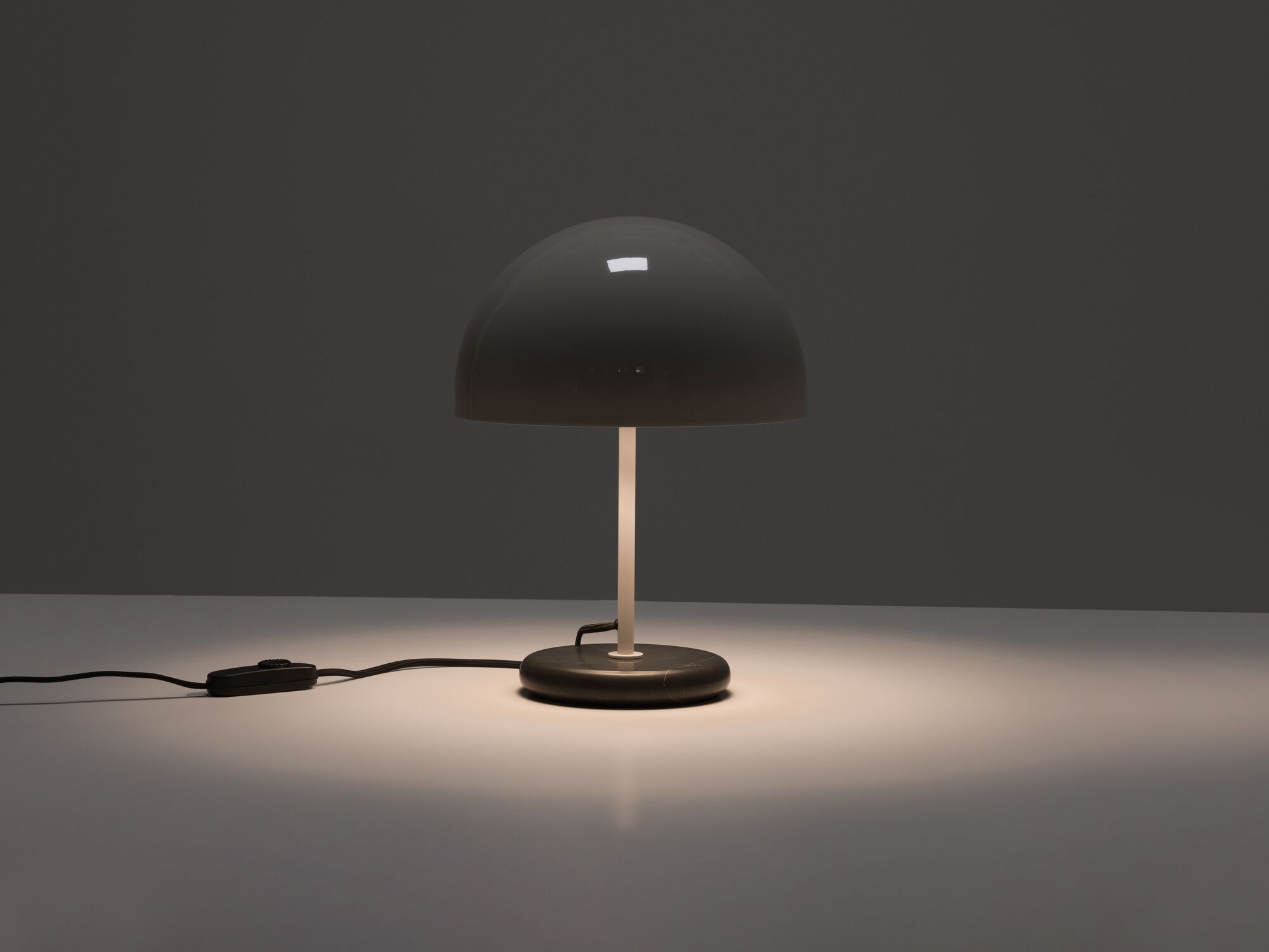 Round grey shade table lamp with light on in the dark front view